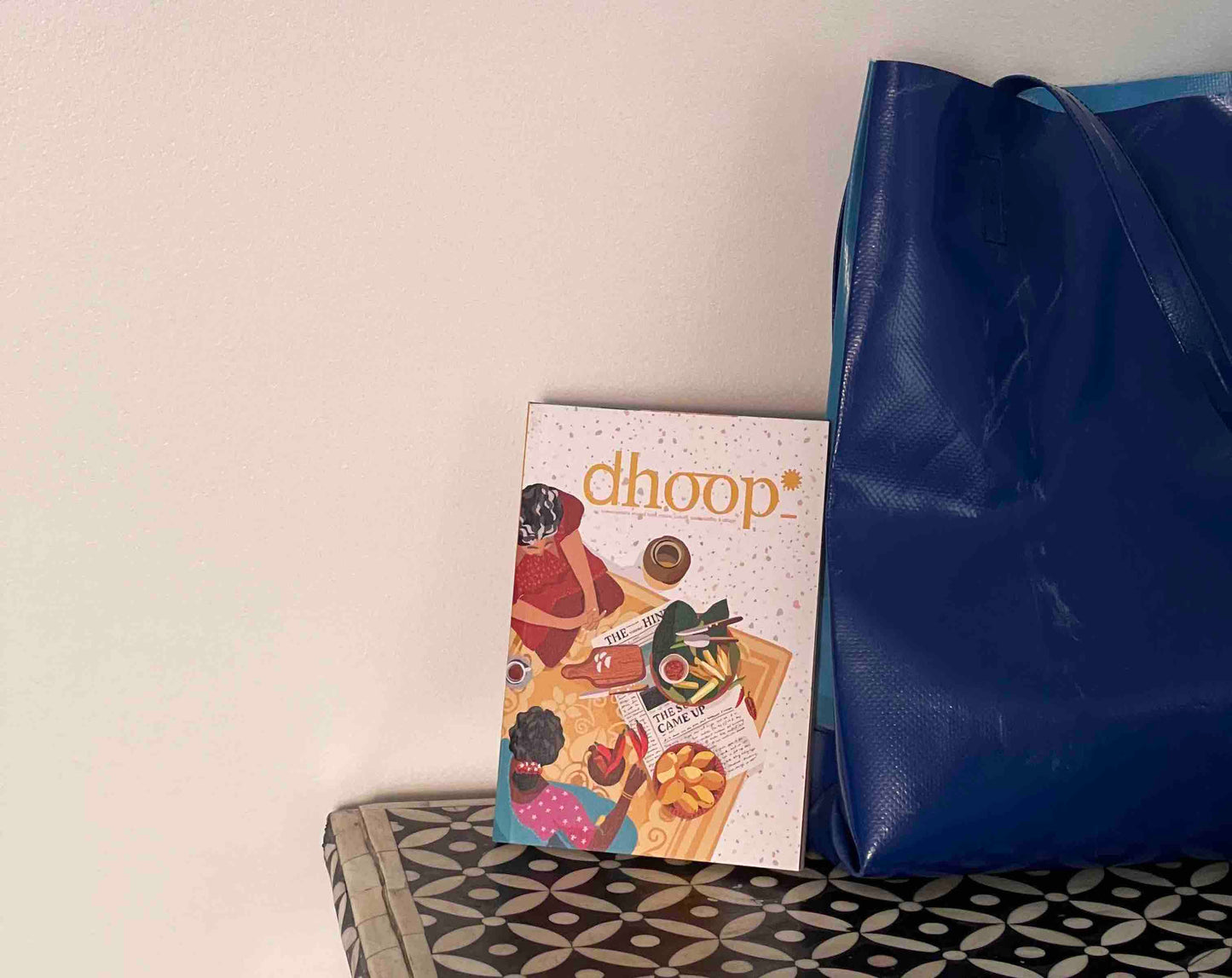 dhoop Magazine lying upright against a big blue bag